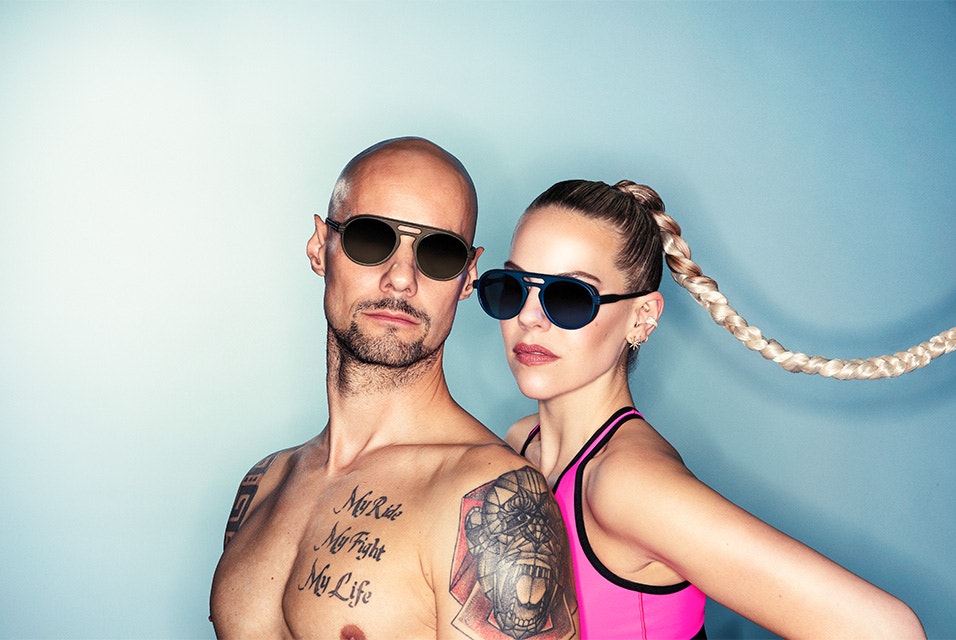 A topless male model and female model in athletic wear posing while wearing 3D-printed sunglasses