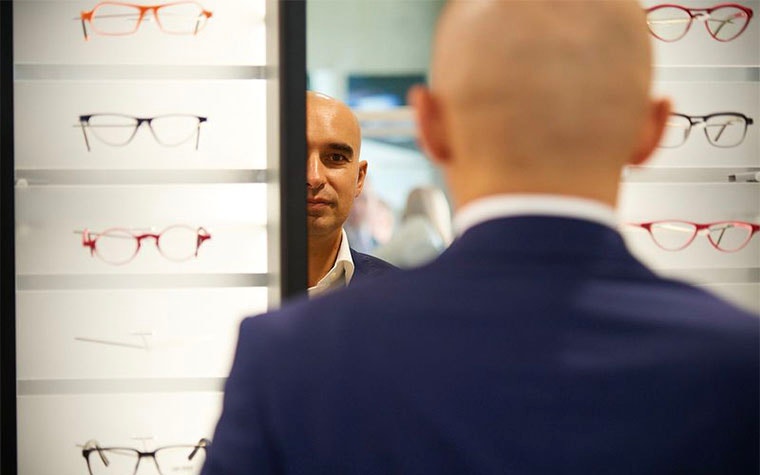Man looking in a mirror next to shelves of eyeglasses
