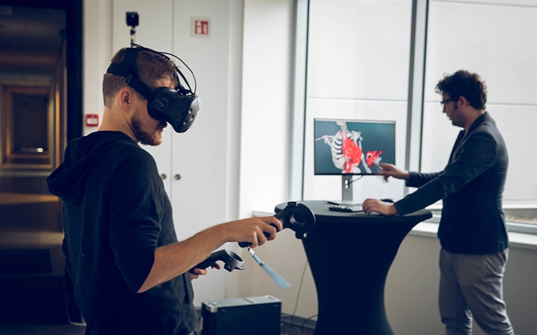 Mann, der Virtual-Reality-Technologie verwendet, während ein anderer Mann den Prozess auf einem Bildschirm beobachtet