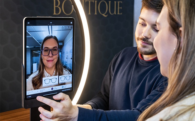 A man and a woman use the Eyewear Fitting Suite on an iPad. The screen shows her face, wearing generated 3D-printed eyewear.