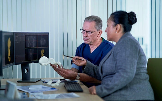 Two people comparing a 3D-printed anatomical model to software on a computer