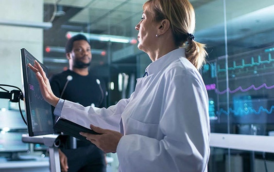 Mujer tocando una pantalla táctil en un laboratorio de investigación con un hombre detrás de ella