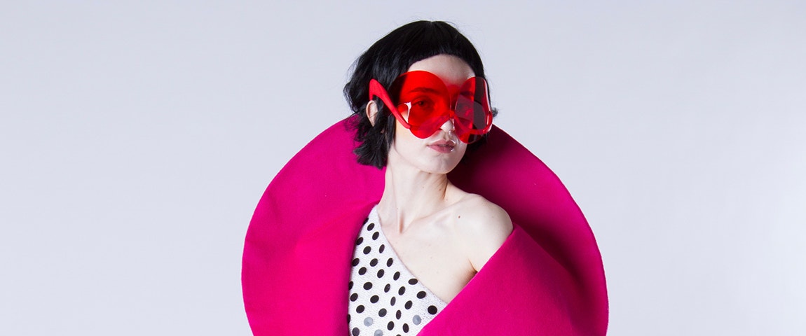 Model wearing a polkadress top, pink shawl, and red sunglasses designed by David Ring