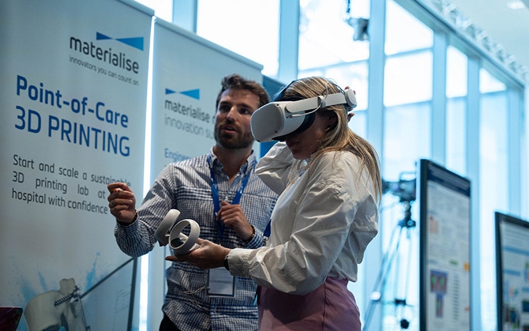 A man assisting a woman wearing a VR headset at a point-of-care 3D printing event