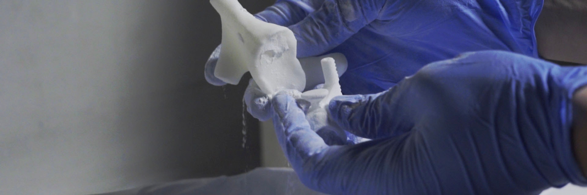 Gloved hands removing a 3D-printed piece from a powder bed