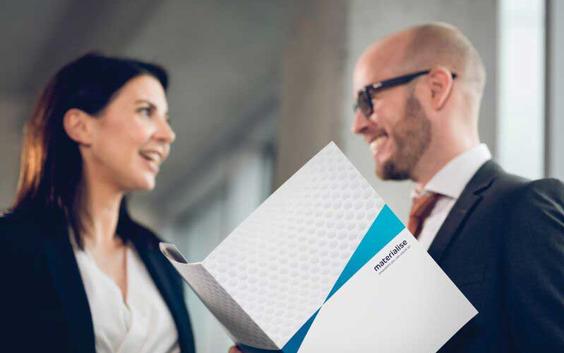 Two people talking and smiling while holding a Materialise folder