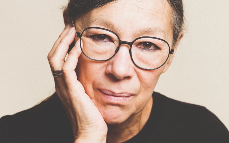 Older female model wearing 3D-printed glasses and posing with her hand on her face