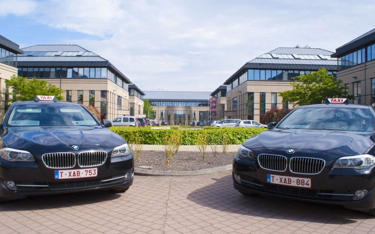 Two black BMW taxis oustide a building complex