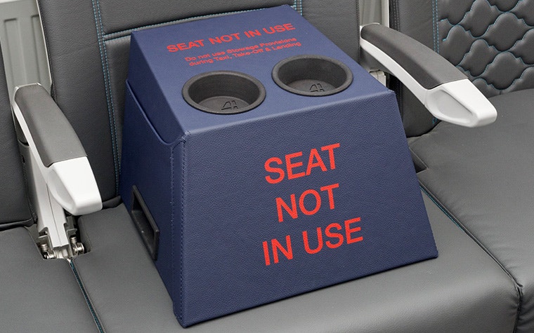 La primera generación del bloqueador de asiento en forma de cubo de Stirling Dynamic, con cuero azul y un portavasos negro impreso en 3D en la parte superior. Las palabras "Asiento no utilizado" están escritas en letras rojas en negrita en la cara frontal.