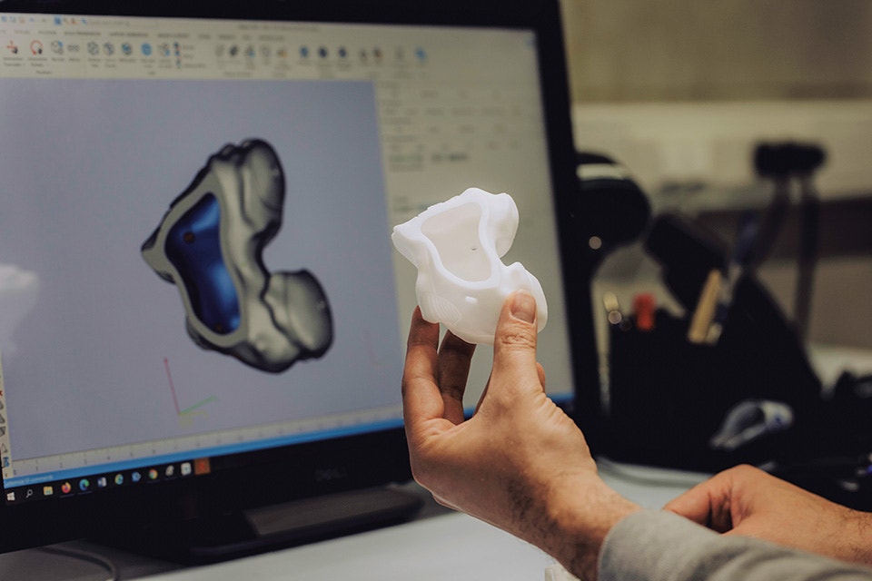 Hand holding a 3D-printed anatomical model in front of a 3D design on a computer