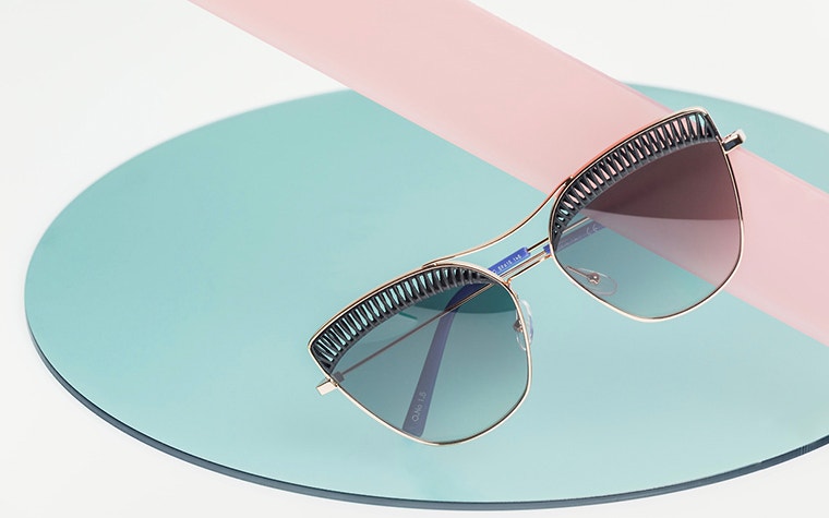 Close-up of stylish, metal, 3D-printed sunglasses with a blue and pink background