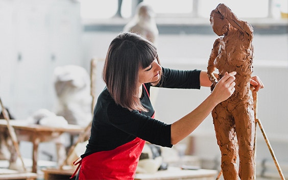 Junge Bildhauerin bei der Arbeit an einer Tonskulptur in ihrem Atelier