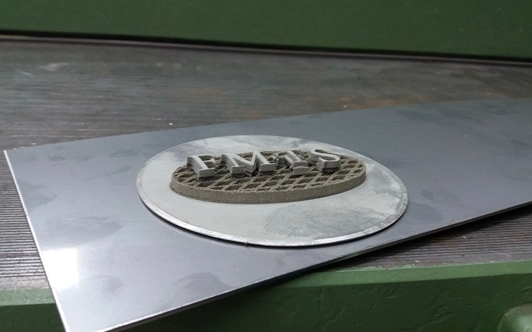 FMTS logo 3D printed in metal on top of a build plate
