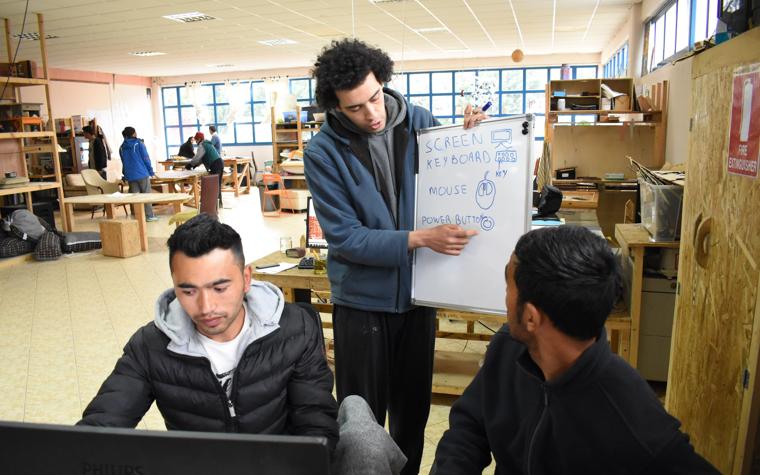 Man explaining parts of a computer to other men with a whiteboard