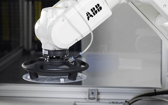 A suction gripper installed on an ABB robot arm, used for assembly tasks on a production line. The gripper is round and black with two visible suction nozzles, and is shown here picking up a flat transparent disk.
