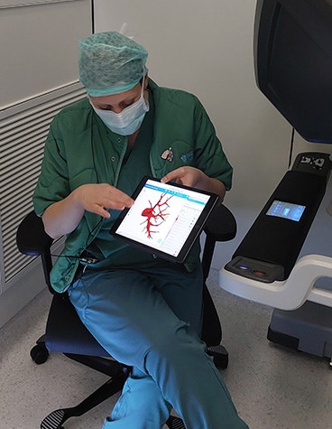 A surgeon in scrubs sitting on a chair and holding a tablet with Materialise Mimics for Thoracic Surgery showing the patient anatomy.