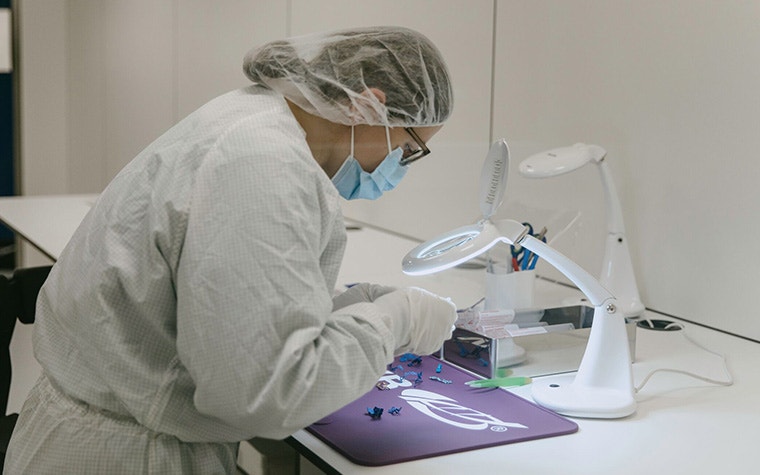 A person in protective gear working on 3D-printed parts in a clean room.
