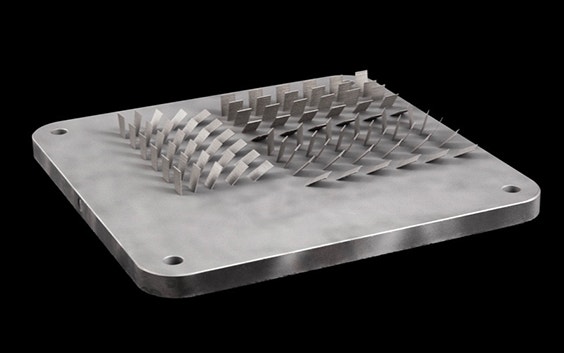 3D-gedruckte Metallproben in verschiedenen Ausrichtungen auf einer Bauplatte.