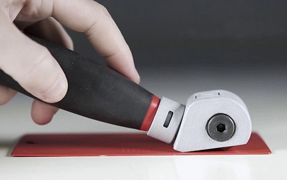 Una mano che trascina l'utensile da taglio di NEURTEK su una lastra di metallo rossa.