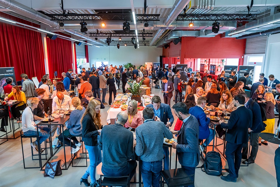 Large group of people at the 3D Printing in Hospitals Forum in Leuven, Belgium, scattered throughout a room at various tables and booths