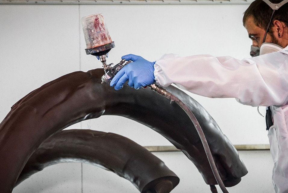 Materialise employee wearing protective equipment spray-paints 3D-printed bone in a brown color 
