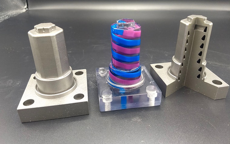 Two metal 3D-printed parts next to a clear printed part with blue and purple swirls