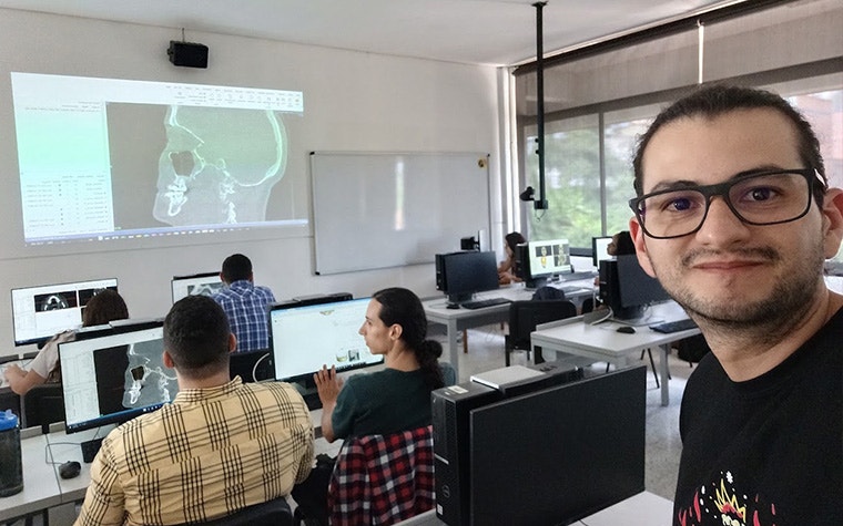 Nicolás Buitrago is taking a selfie image. He is looking at the camera  and in the background is a classroom full of students using Materialise Mimics.