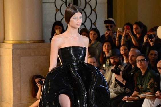 Model on a runway wearing a shiny, 3D-printed dress that bubbles out at the hips