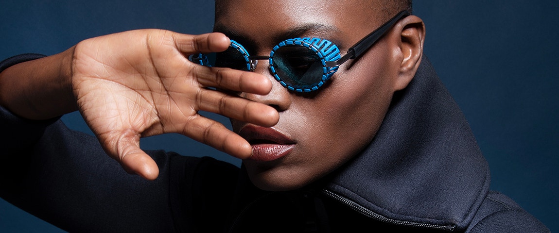 Black female model posing with her hand in front of her face while wearing blue sunglasses from the JFRey Nautinew collection