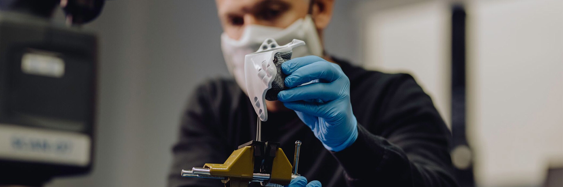 Ein Mann mit blauen Latexhandschuhen misst vorsichtig ein 3D-gedrucktes Teil aus