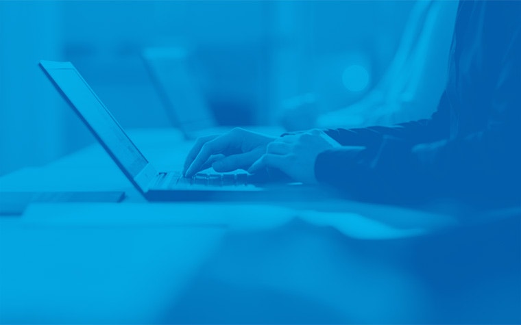 A person typing on a laptop with a blue filter over the image.