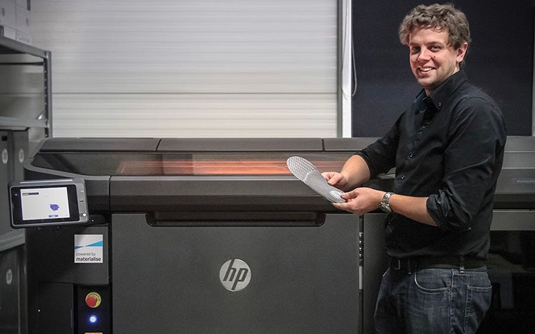 Giovanni Vleminckx stands beside a HP Multi Jet Fusion printer holding a 3D-printed insole