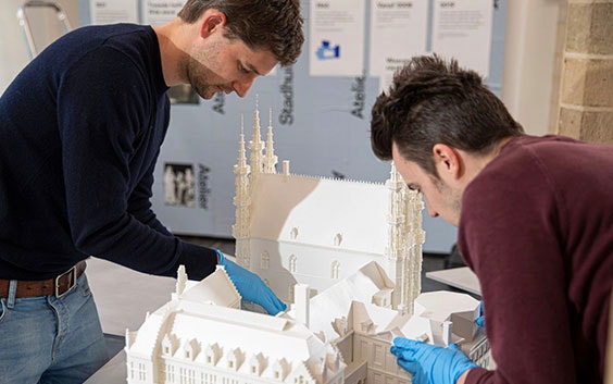 Two people assembling a 3D-printed model of the Leuven city hall