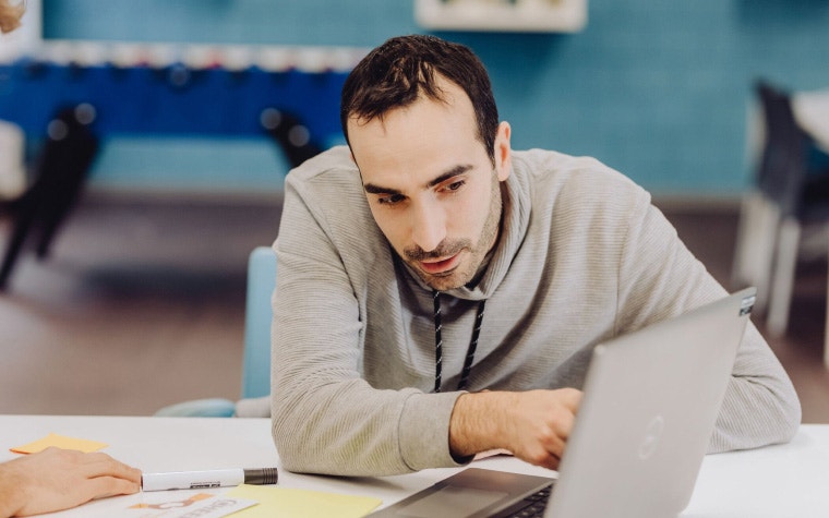 A project engineer sitting at a table and pointing at the screen of a laptop