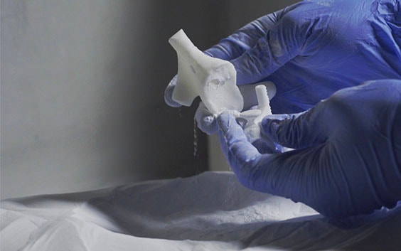 Gloved hands removing a 3D-printed piece from a powder bed