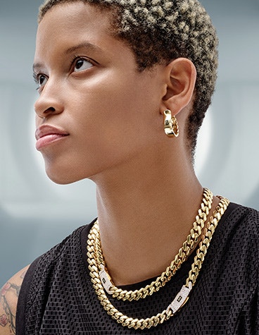 黒いショートパンツ姿で左を見つめる女性。耳には金のイヤリング、太い金のチェーンを3本つけている。