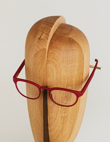Top view of red Yuniku+Ørgreen eyeglasses on a wooden stand