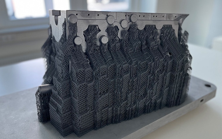 A metal 3D-printed crankcase produced by the BÖLLINGER GROUP sitting on a wooden table.