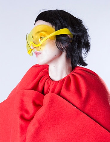 La modella indossa un abito rosso e occhiali da sole gialli e artistici disegnati da David Ring.