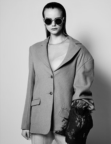 Image lointaine en niveaux de gris d'un modèle féminin portant des lunettes de soleil rondes de la collection BAARS x GOGOSHA