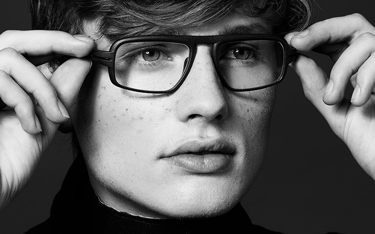 Close-up, gray-scale image of a male model holding Hoet Cabrio PZ eyeglasses to his face