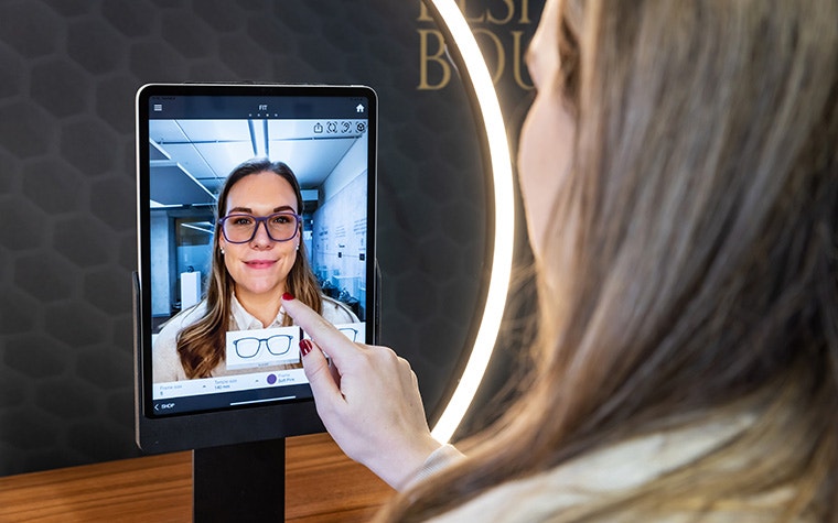 A woman uses the Eyewear Fitting Suite on an iPad. The screen shows her face, along with a generated image of 3D-printed eyewear.