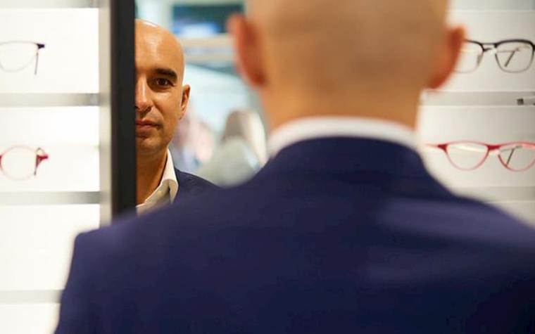 Man looking in a mirror next to shelves of eyeglasses