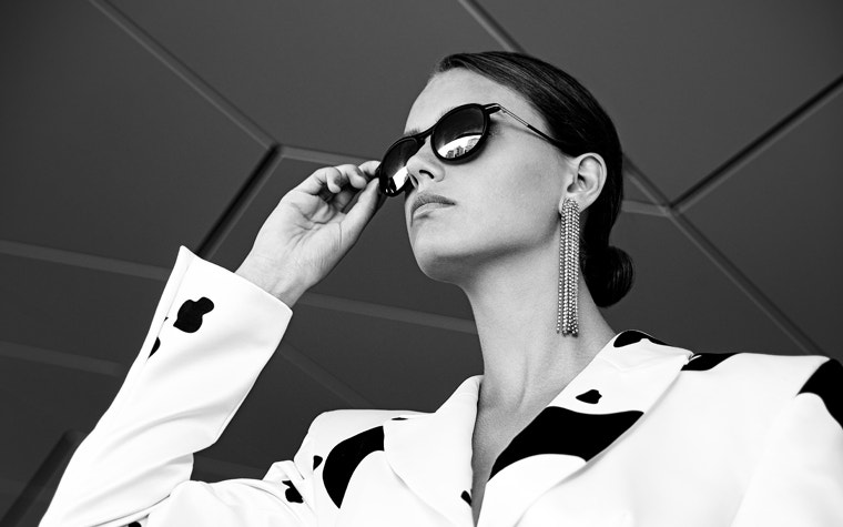 Graustufenbild eines weiblichen Modells, das nach oben blickt und eine Sonnenbrille aus der Hoet Cabrio PR-Kollektion hält und trägt