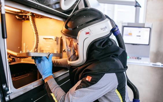 Man wearing safety gear and removing a 3D-printed build from a 3D printer