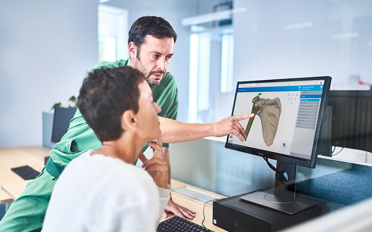 Two medical practitioners discussing a CAD image of a medical model on a computer screen.