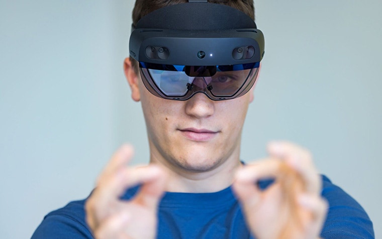 Man wearing Microsoft HoloLens AR googles and holding his hands out in front of him in a pinching gesture