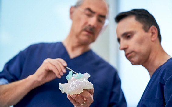 Two men dressed in hospital scrubs, looking at a 3D-printed anatomical model