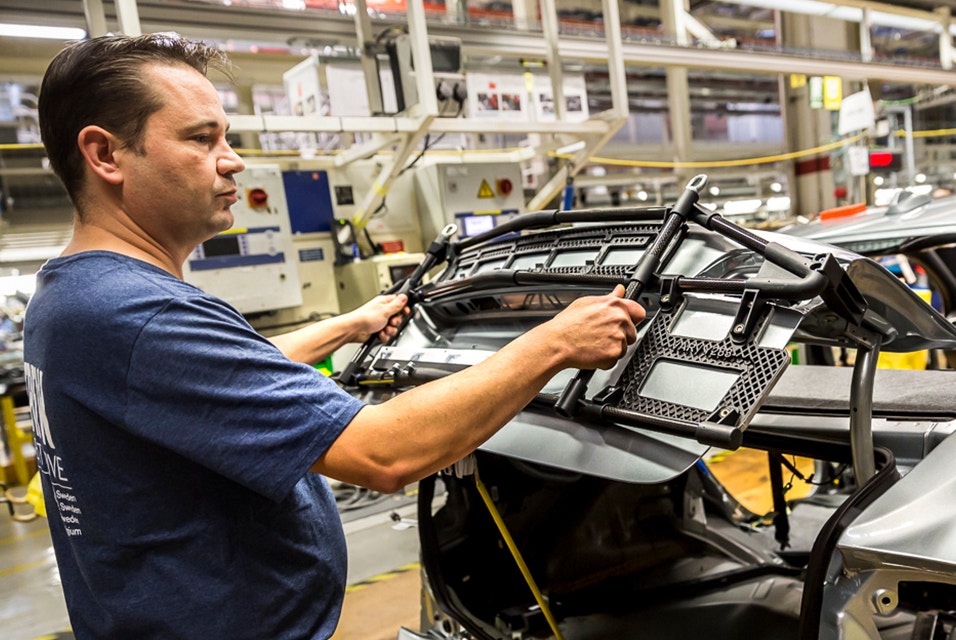 A worker at Volvo using a 3D-printed gluing jig to affix the Volvo logo and key information to the trunk of each new car