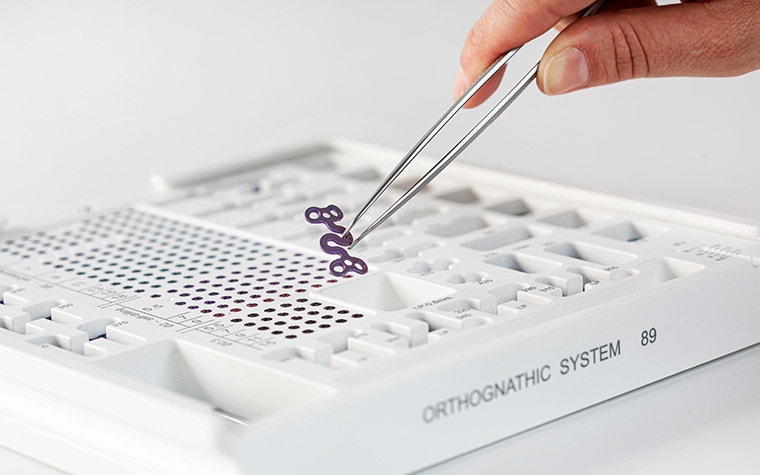 Hand picking up an S-plate from the orthognathic system set with tweezers